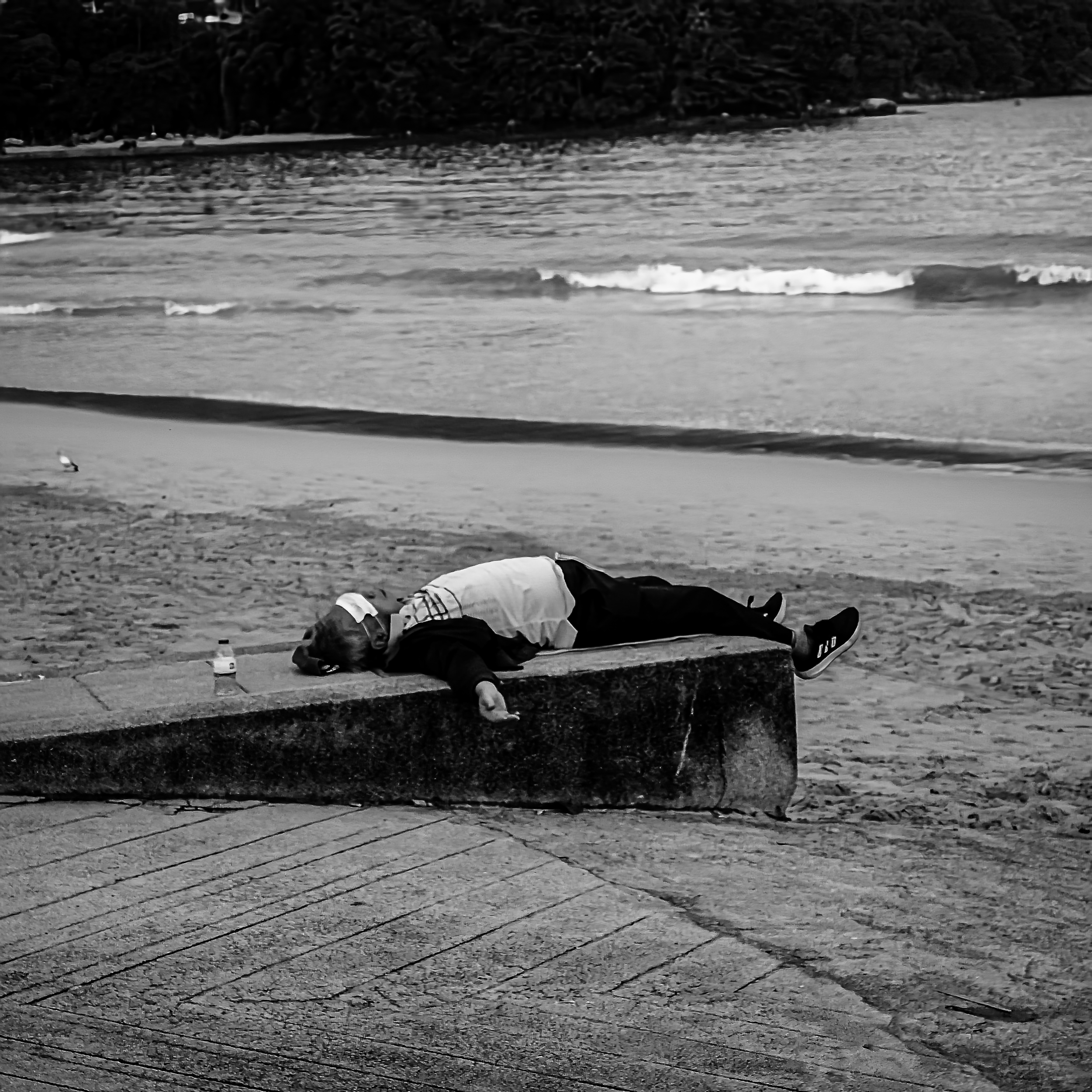 A solitary man sleeping on a concrete platform beside the sea