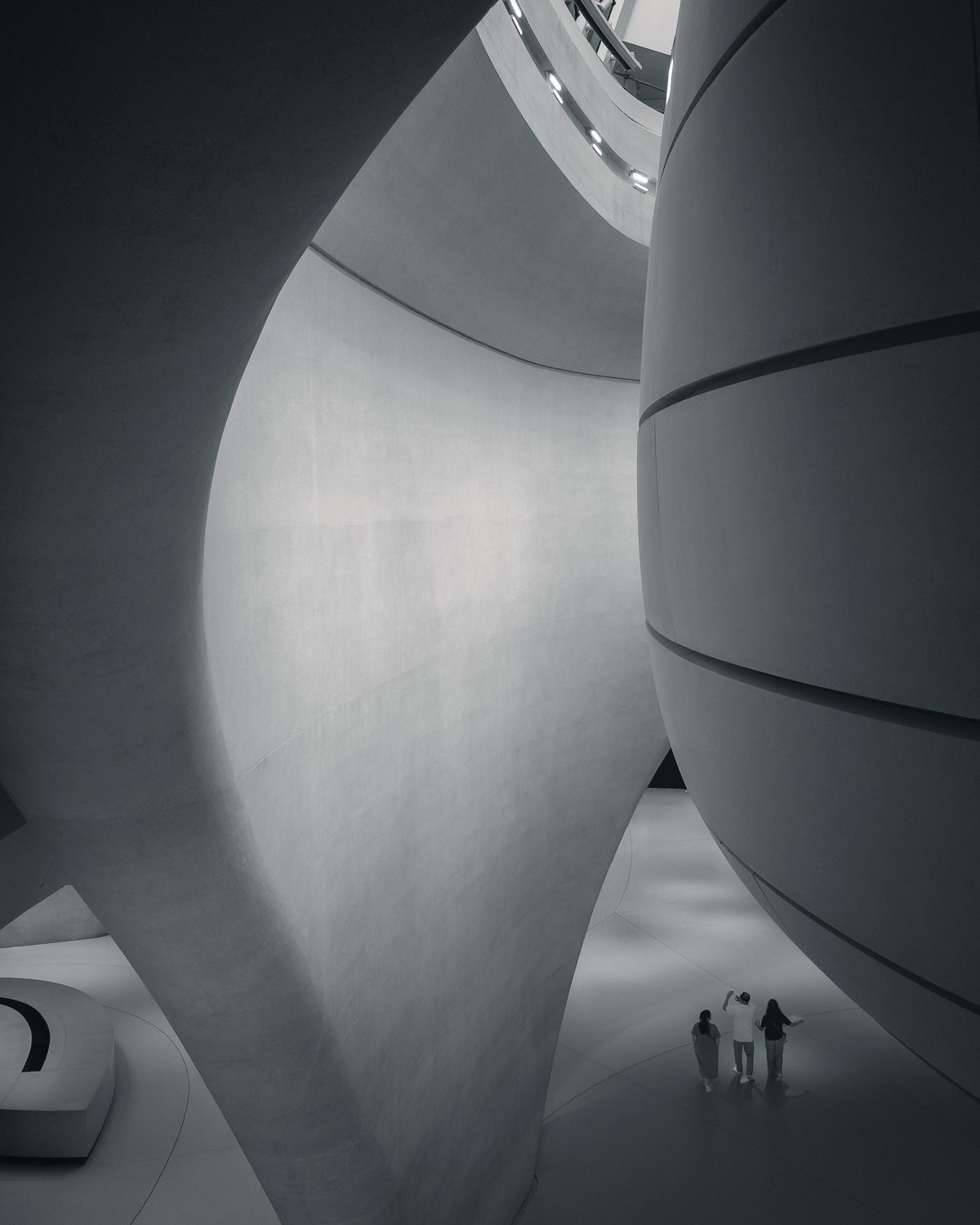 Three small figures beneath sweeping curved concrete walls in a vast white interior