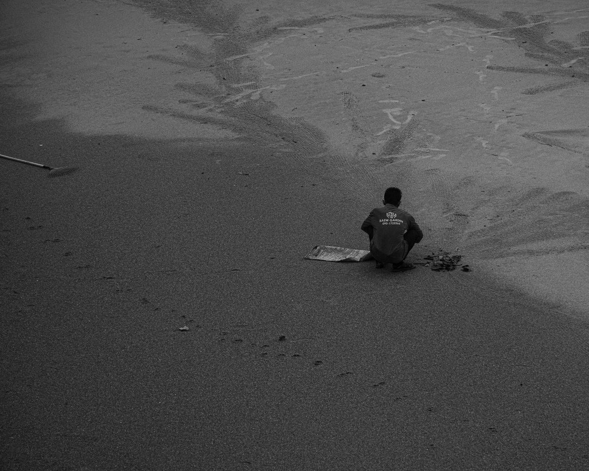 A man crouches alone on a wide stretch of wet sand marked with drawings