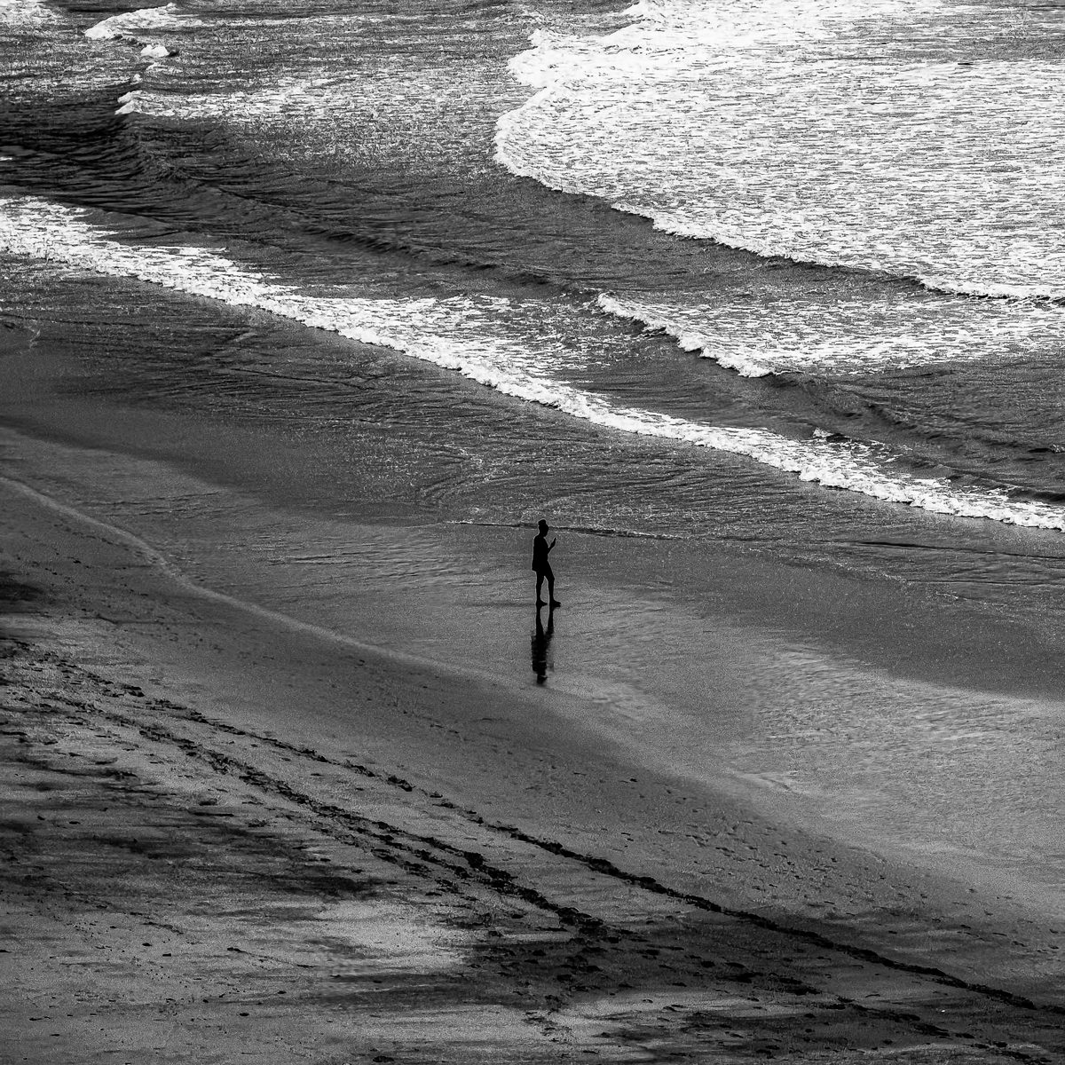 Seen from above, one person walks along a beach beside breaking waves