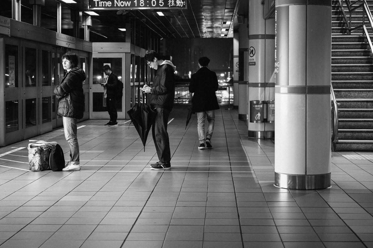 Commuters wait apart from each other on a station concourse