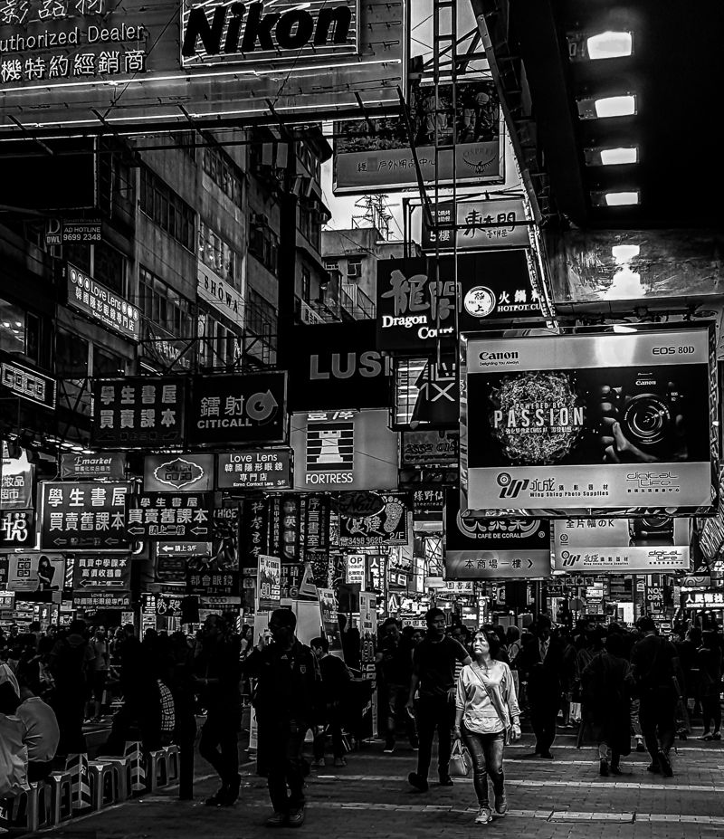 A woman walks through a dense crowd under stacked neon shop signs