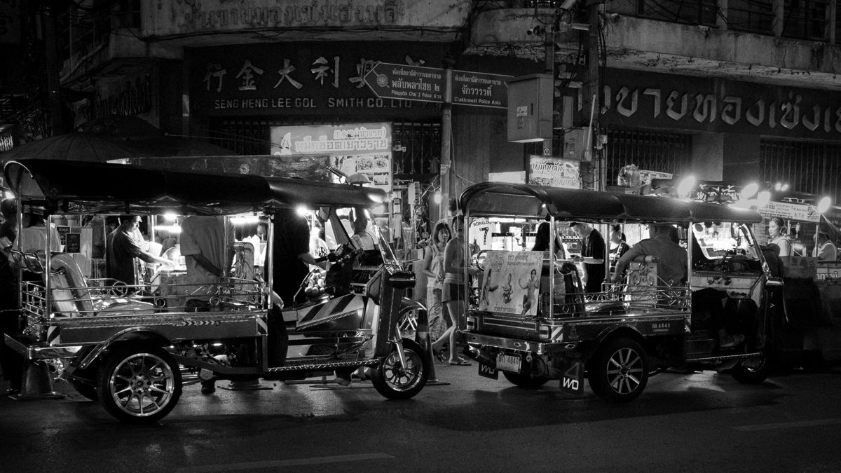 Two tuk-tuks wait under shop signs on a street at night